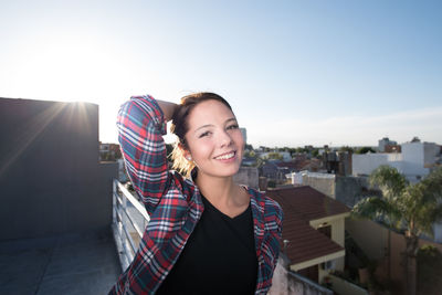 Portrait of smiling young woman in city against sky