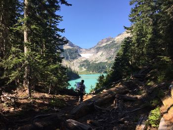 Rear view of man with backpack walking towards lake against sky