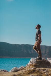 Side view of young woman standing on rock against sea