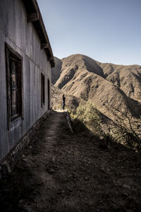 Rear view of man walking on road along built structures