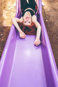 High angle portrait of young woman sliding on purple slide in playground