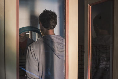 Rear view of man standing by window