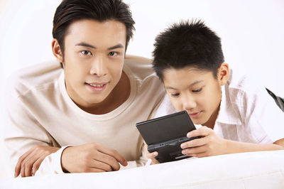 Father and son using mobile phone against wall at home