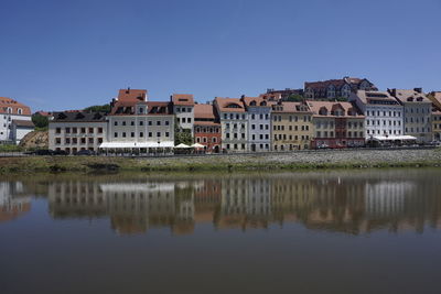 Buildings by river against blue sky