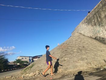 Side view of woman on road against blue sky