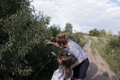 Mother and daughter picking fruits on plant against cloudy sky