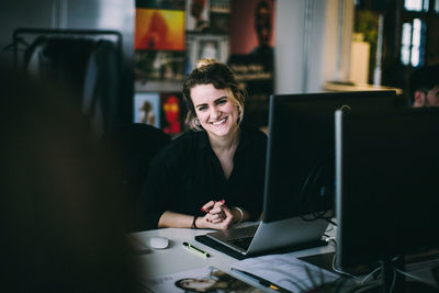 Portrait young woman smiling while sitting at desk in creative office