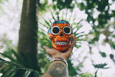 Cropped hand of man holding skull against trees