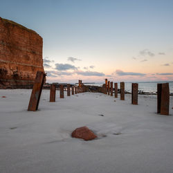 Wooden posts on beach against sky during sunset