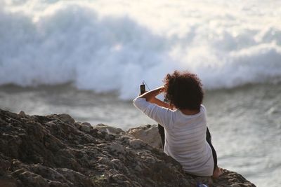 Rear view of woman photographing against sea