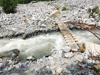 High angle view of footbridge on stream flowing through rocks