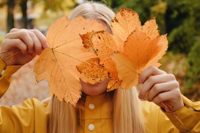 Portrait of person hiding behind autumn leaves, holding leaves in front of face