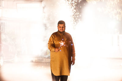 Man holding lit sparkler while standing at night during diwali
