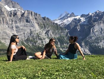 Friends sitting on mountain against sky