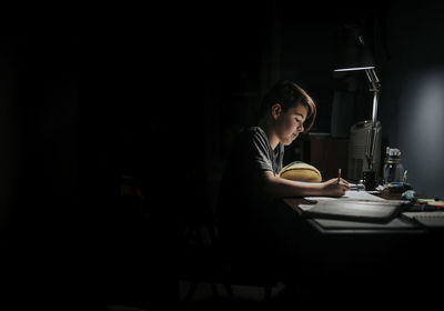 Side view of boy studying at table in darkroom
