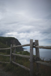 Barbed wire fence on field against cloudy sky