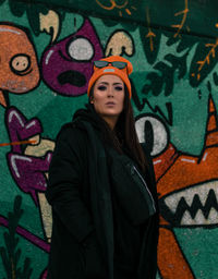 Portrait of young woman standing against graffiti wall