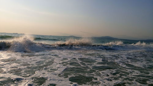 Waves splashing in sea against sky during sunset