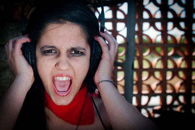 Portrait of woman wearing headphones shouting while standing against window