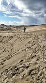 Man walking on sand dunes against sky