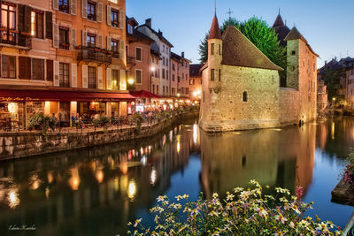 Canal by illuminated city against sky