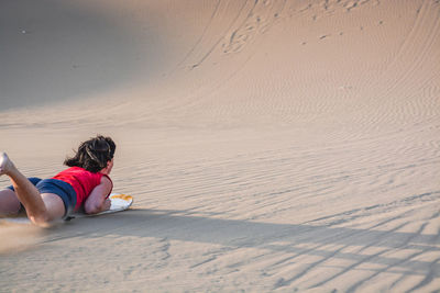 Rear view of woman sandboarding on sand dune