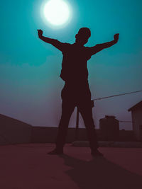 Silhouette man with arms outstretched standing against sky