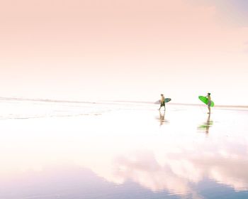 Men with surfboards walking on seashore at beach against sky