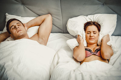 High angle view of woman covering ears with pillow while man snoring on bed