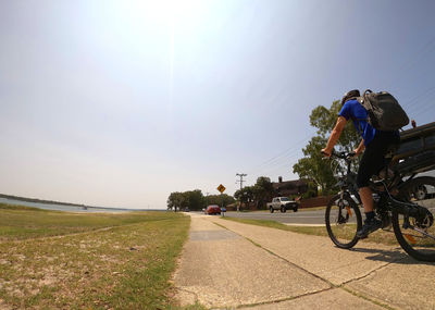 Rear view of people riding bicycle on road against sky