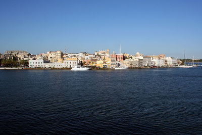 Sea by cityscape against clear blue sky