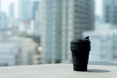 Close-up of coffee cup on table against buildings in city