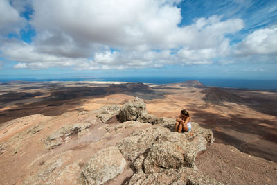 Woman on rock by mountain against sky