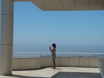 Rear view of woman standing on balcony against clear blue sky
