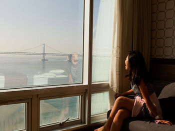 Woman looking through window while sitting on sofa at home