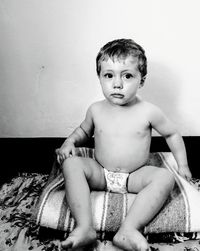 Portrait of shirtless boy sitting against wall at home