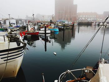 Boats moored at harbor against sky in city