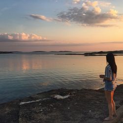 Rear view of woman standing at beach during sunset