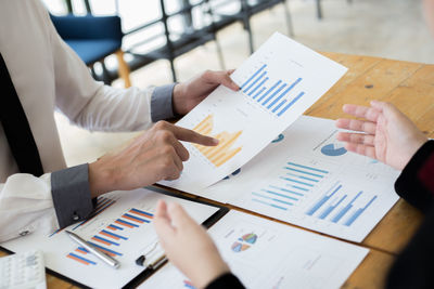 Cropped image of business colleagues analyzing graph on desk in office