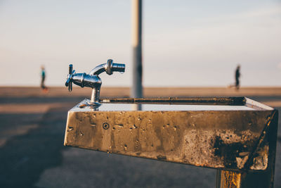 Close-up of faucet by road against sky