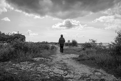 Rear view of man walking on landscape against sky