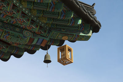 Low angle view of lantern hanging on roof of temple against clear blue sky