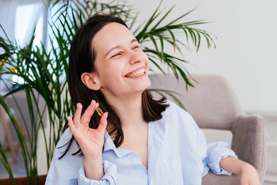 Smiling young woman with short hair holding pill omega capsule in hand at home. girl taking medicine