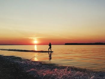 Silhouette person standing on beach against sky during sunset