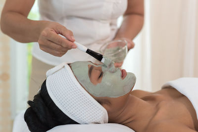 Midsection of beautician applying facial mask on woman face at spa