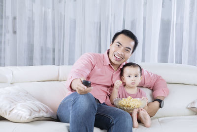 Father with daughter eating popcorn while sitting on sofa at home