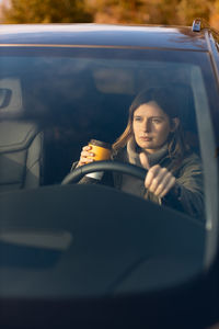 Young girl in the morning goes to work by car and drinking coffee. view through the windshield. 