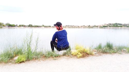 Rear view of man sitting at lakeshore against sky