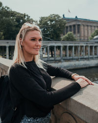 Young woman looking away while standing by retaining wall in city