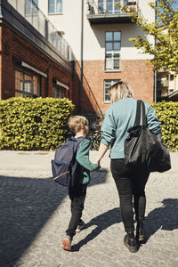 Rear view of mother walking with son towards school building on sunny day